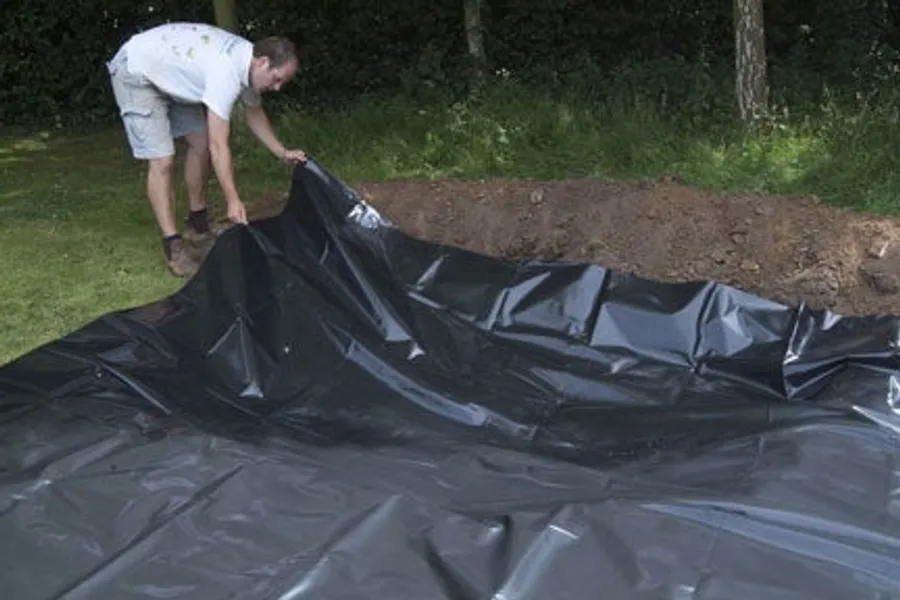A flexible pond liner sheet being positioned in a dug pond